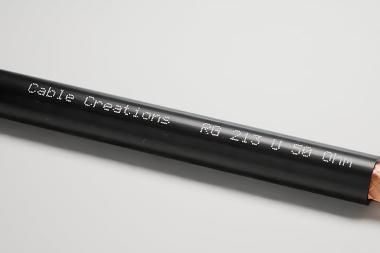 3D-Rendering: Nahaufnahme des Aufdrucks auf dem Mantel – Koaxialkabel RG 213 mit schwarzem Mantel, Kupfergeflecht, weißer Isolierung und verseiltem Kupferleiter, im Fotostudio auf hellem Grund, Aufdruck „Cable Creations“