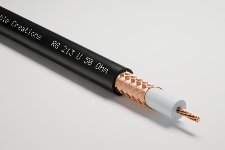3D-Rendering: Dreiviertelansicht des abgesetzten Endes – Koaxialkabel RG 213 mit schwarzem Mantel, Kupfergeflecht, weißer Isolierung und verseiltem Kupferleiter, im Fotostudio auf hellem Grund, Aufdruck „Cable Creations“