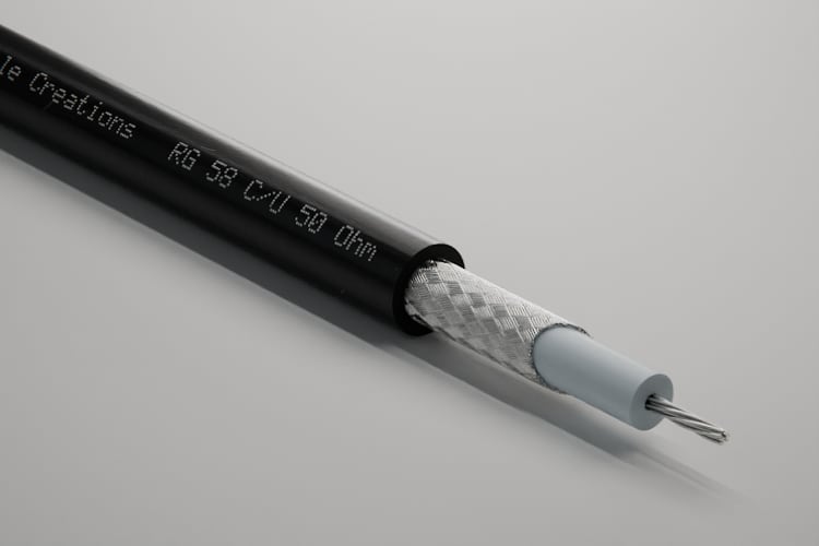 3D-Rendering: Dreiviertelansicht des abgesetzten Endes – Koaxialkabel RG 58 mit schwarzem Mantel, verzinntem Geflecht, heller Isolierung und verseiltem Leiter, im Fotostudio für blankes Metall, Aufdruck „Cable Creations“